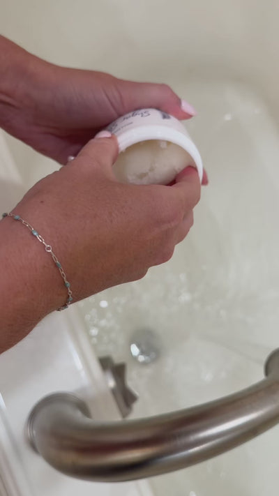 hand scooping sugar scrub out of jar and moving it in hand to show the texture over the water running